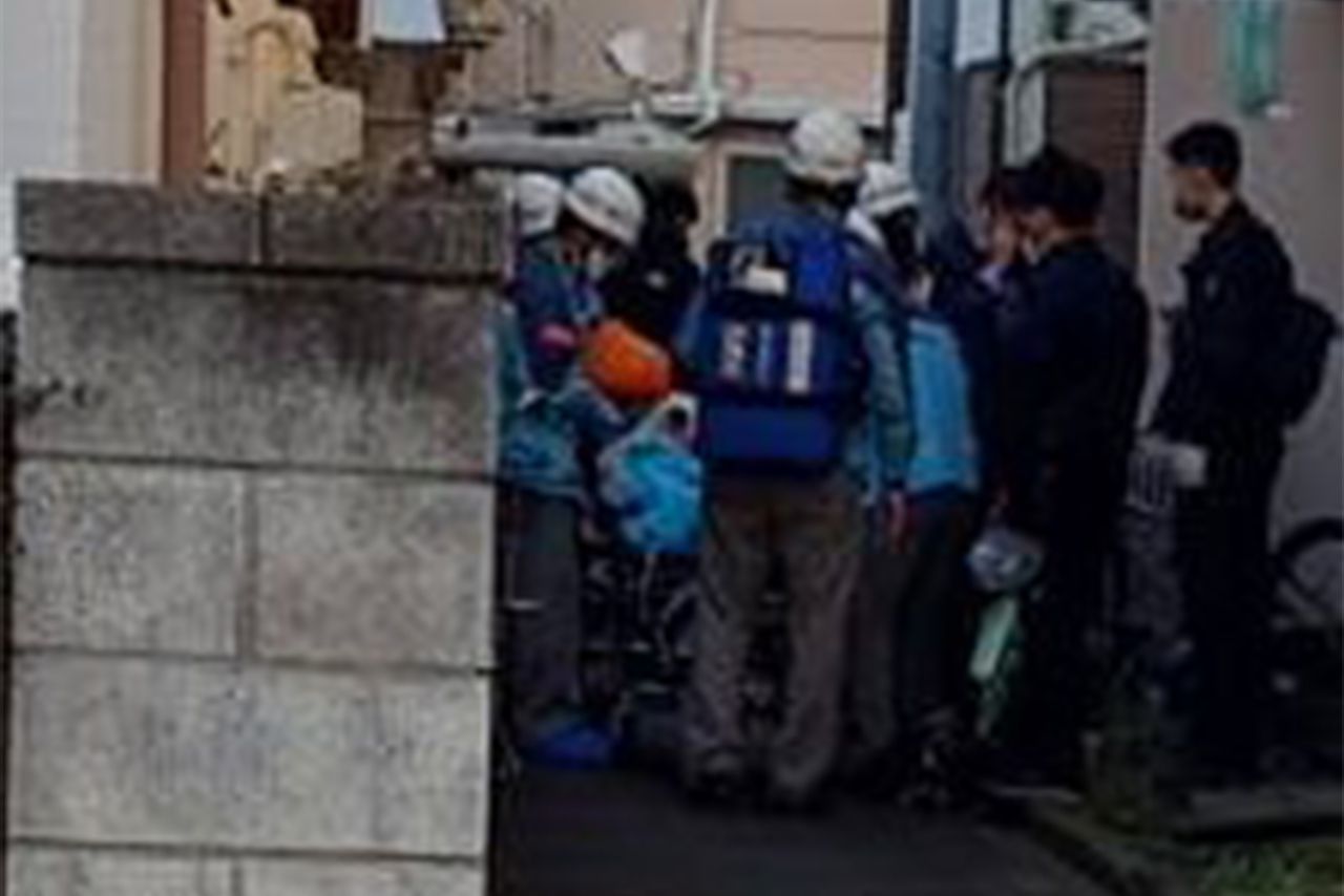 逮捕前、座布団に火をつけるなどしてケガをし、ストレッチャーで運ばれる宮哲夫容疑者（写真左側の白いフードをかぶった人物＝目撃者提供）