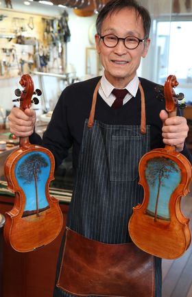 津波ヴァイオリンとヴィオラを持つ中澤氏。裏には“奇跡の一本松”の絵が描かれている