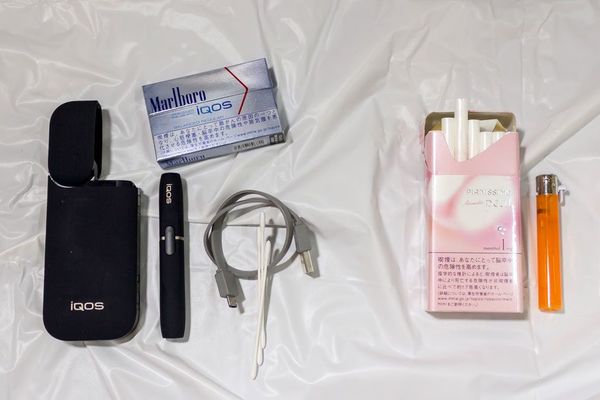 右側が従来の紙巻きタバコとライター。左側が専用ヒートスティック、アイコス本体、ポケットチャージャー、充電用のケーブル、綿棒