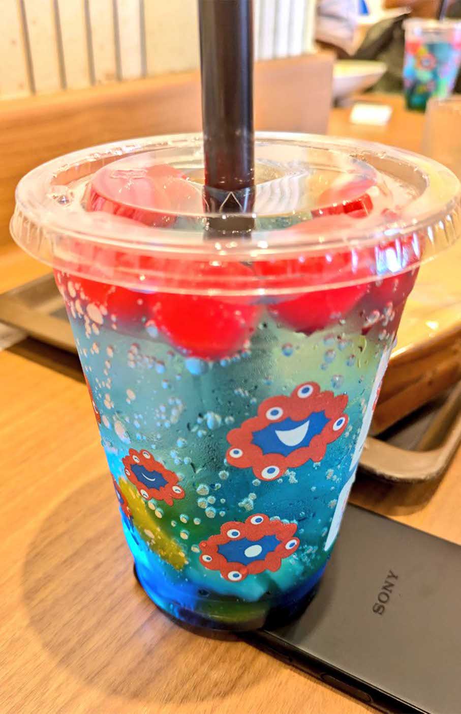 エスタシオンカフェにて販売されている『ミャクミャクフルーツソーダ』。青いソーダに真っ赤なチェリーが浮かぶ（Xより）