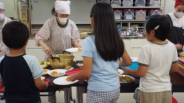 ボランティアがよそう料理を子どもたちが自分で取りにいく