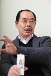 大好きな牛乳を片手に自身の事務所でインタビューに応じる野田義治氏(撮影:竹内摩耶)