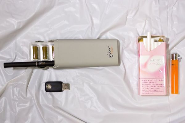 右側が従来の紙巻きタバコとライター。左側が専用たばこカプセル、プルーム・テック本体、専用ケース、充電用USBアダプター