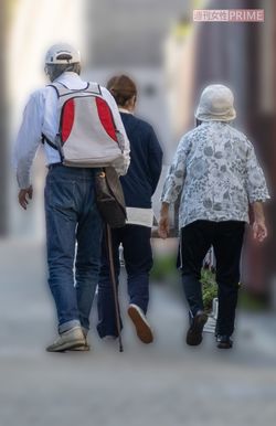 ヘルパーに付き添われた妻のひかるさん（右）に寄り添い、杖をつきながら散歩に向かった山崎（左）