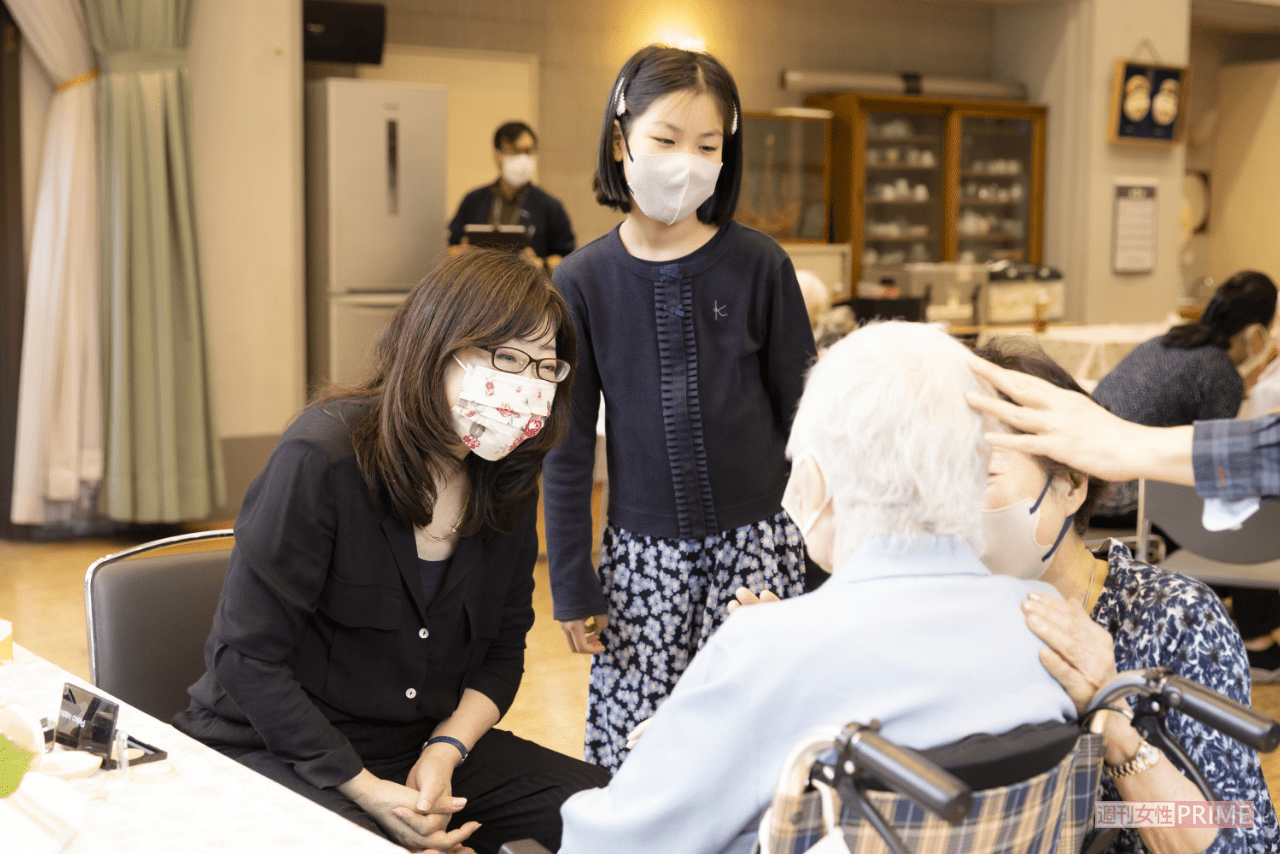 〇〇ちゃんと高齢者の名前を呼んで笑顔を引き出し、緊張を一瞬でほぐすかづきさん。万博やボランティアには孫（右隣）が見学に訪れ、その仕事ぶりを「カッコいい」と絶賛（撮影／矢島泰輔）