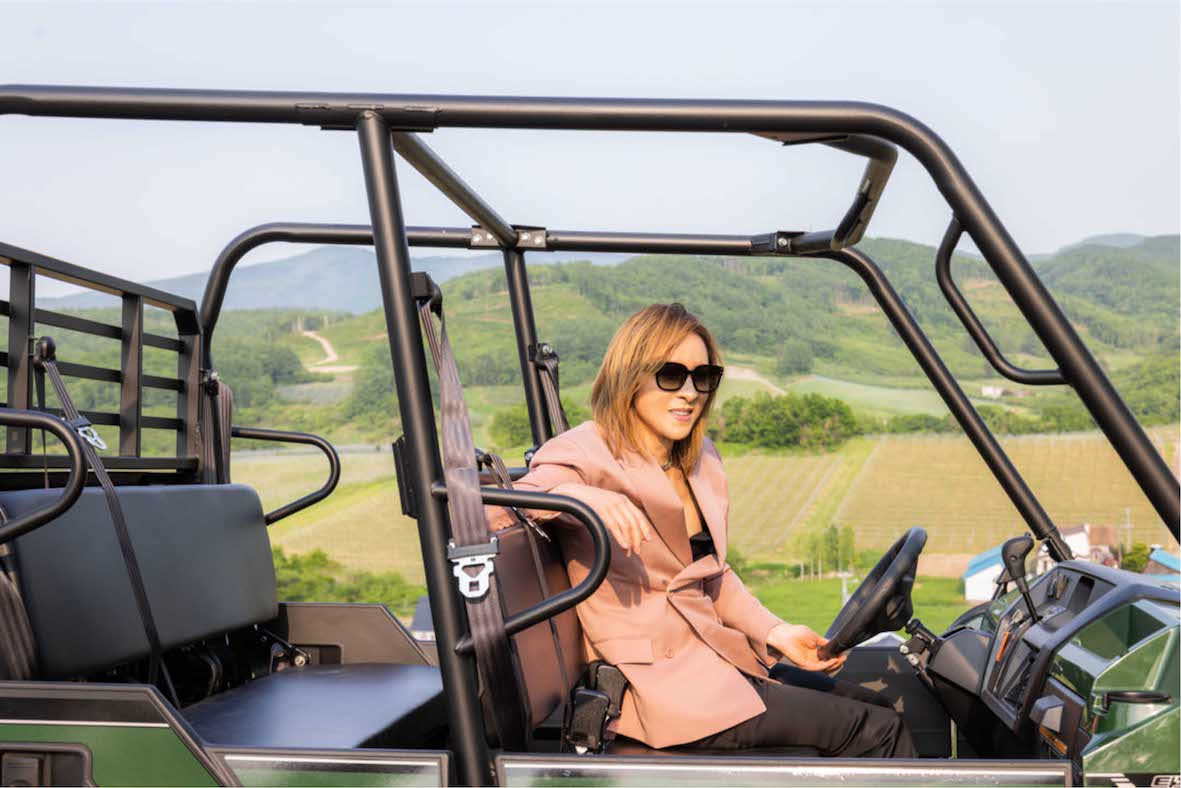 初となる日本産ワインプロジェクトを始動し、北海道を訪れピンクのジャケットとパンツスタイルで畑作業に挑戦したYOSIHIKI（『YbyYOSHIKI』公式サイトより）