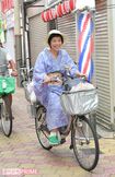 帽子に着物姿で自転車にまたがり、商店街を颯爽と走る