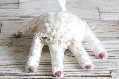 【ポップコーンハンド】ポリエチレンの手袋を用意。指先の部分にマーブルチョコ（赤）を1個ずつ詰める。ポップコーンを手首の手前ぐらいまで詰めたら、手首部分を結んで留める。　『可愛くって ホラーで 美味しい！ キモめし』より