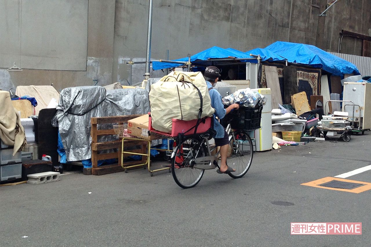 大量な空き缶を積んで自転車をこぐホームレス