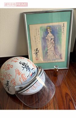 仲代達矢さんの落書きで埋め尽くされた岡本真実さんのヘルメット。後ろの絵は、奥さんの恭子さんが描いた真実さんの似顔絵