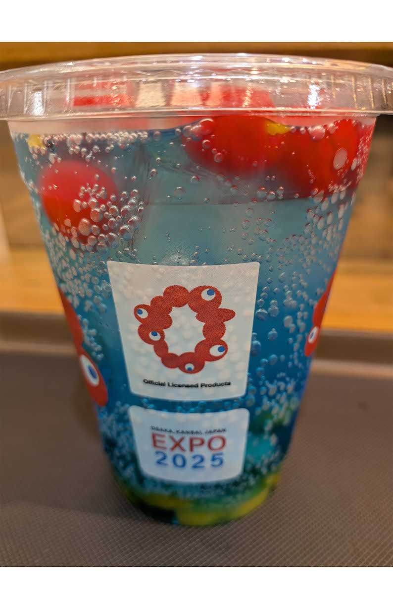 エスタシオンカフェにて販売されている『ミャクミャクフルーツソーダ』。青いソーダに真っ赤なチェリーが浮かぶ（Xより）