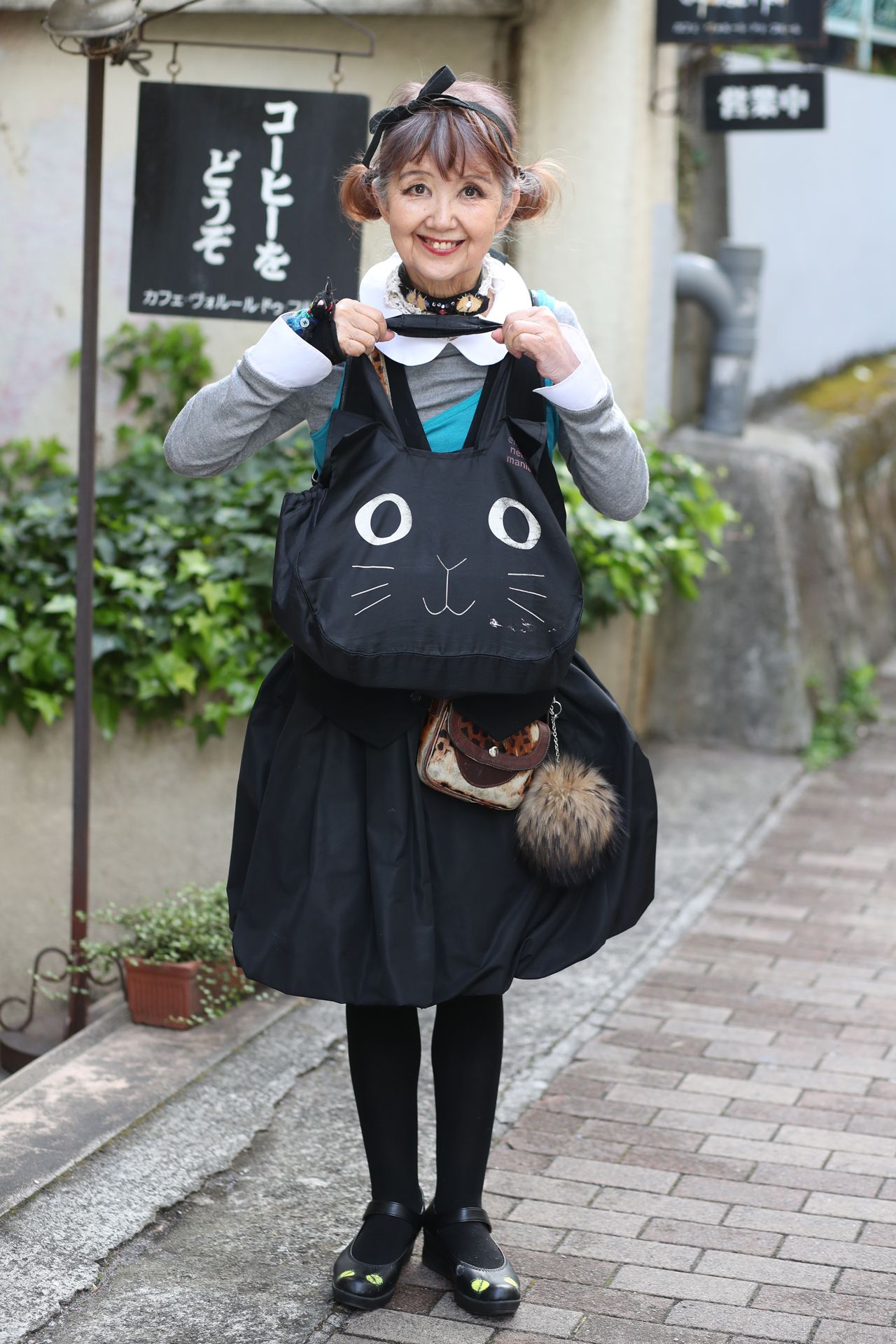 お手製のぬいぐるみや小物を身につけ、本日は全身黒猫風コーディネート！　お気に入りの喫茶店の前で。　撮影／坂本利幸