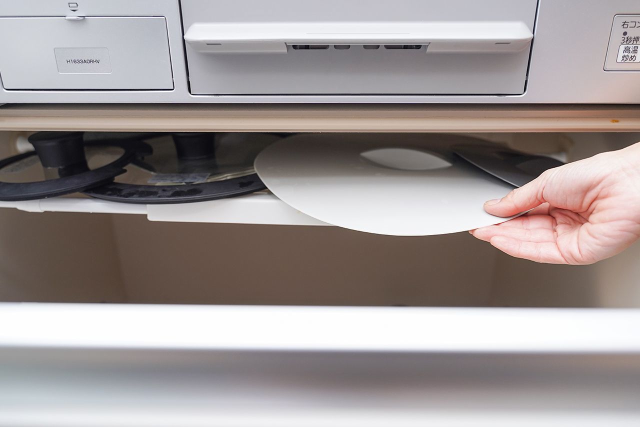 白い伸縮式つっぱり棒、つっぱり棒用棚「コンロ下の引き出し上部にあるスキマに、つっぱり棒で棚を作成。立てて収納しにくいシリコン製の鍋ぶたを収納しています」各110円／ダイソー　写真／フジモリタイシ、ヒラヤマタイジロー（『スキマをうめる収納ルール』より）