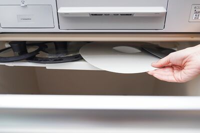 白い伸縮式つっぱり棒、つっぱり棒用棚「コンロ下の引き出し上部にあるスキマに、つっぱり棒で棚を作成。立てて収納しにくいシリコン製の鍋ぶたを収納しています」各110円／ダイソー　写真／フジモリタイシ、ヒラヤマタイジロー（『スキマをうめる収納ルール』より）