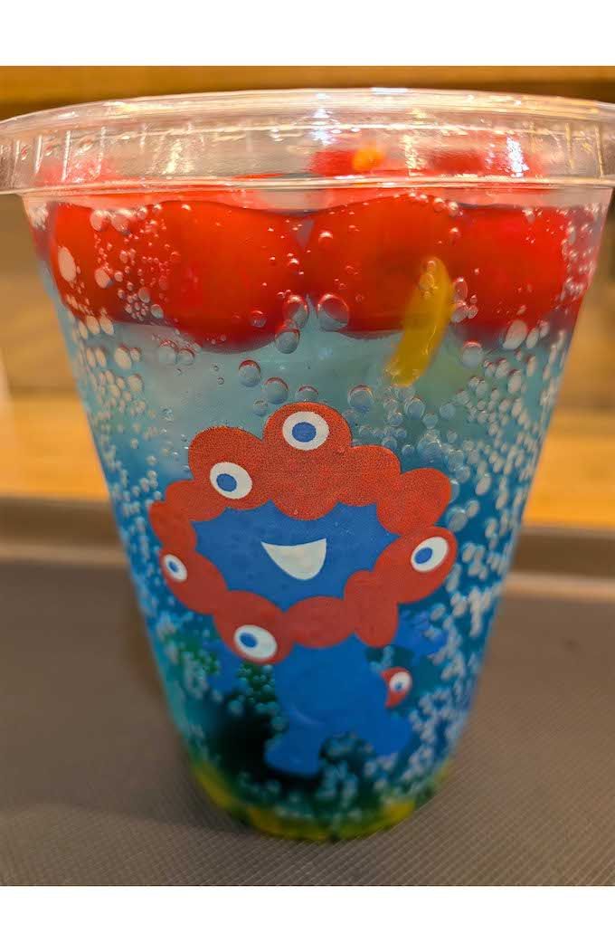 エスタシオンカフェにて販売されている『ミャクミャクフルーツソーダ』。青いソーダに真っ赤なチェリーが浮かぶ（Xより）