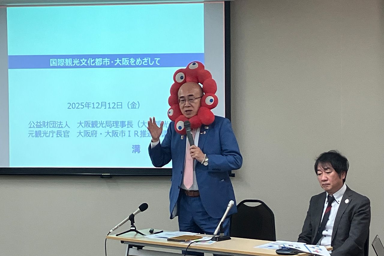 ミャクミャクのぬいぐるみをつけたまま会見をする大阪観光局理事長・溝畑宏さん