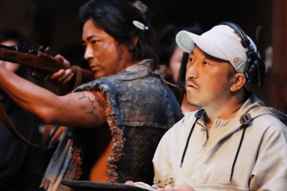 『十一人の賊軍』の撮影現場。爆破の轟音と血しぶきが飛び交うオープンセットの中、鋭い視線でモニターをチェックしながら白石は、「ここに来る山道がワクワクした道に見える」