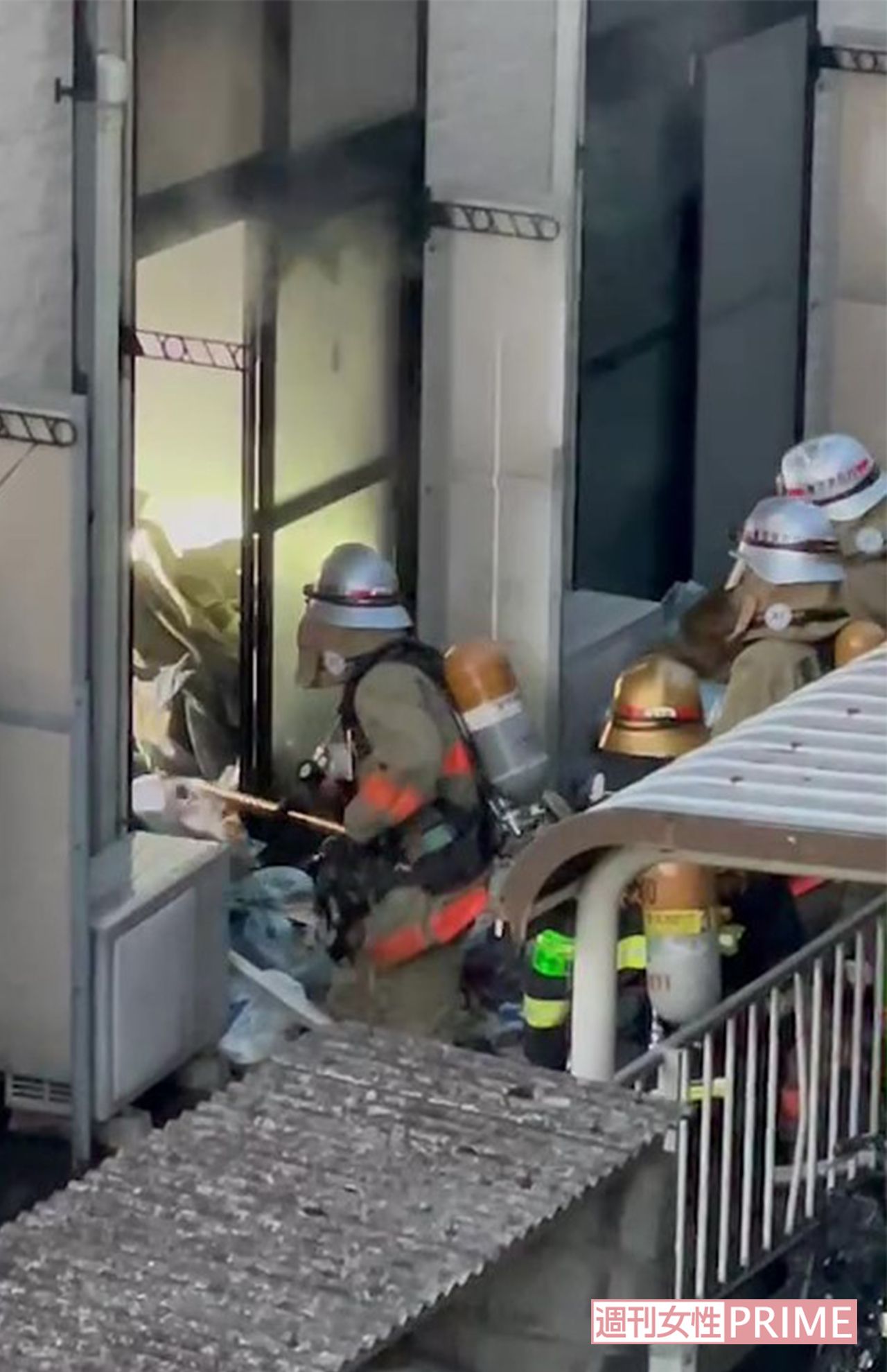 裏手の窓ガラスを割り、田原春貴之容疑者の部屋のゴミを熊手のような棒で掻き出す消防隊員（目撃者提供）