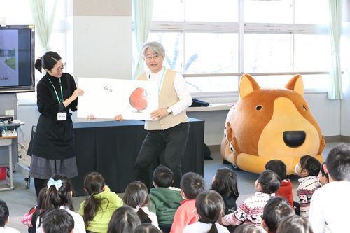 吉成館長の絵本読み聞かせ。身振り手振りで子どもたちを夢中にさせ、楽しませる。右横にあるのが、わんこカート『きらら』