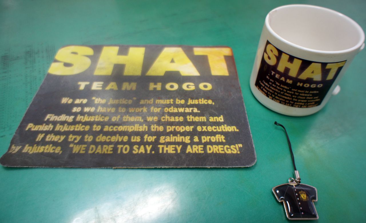 2013年、携帯ストラップ（右手前）を4個作製。2014年、マグカップ（右奥）1個とパソコンのマウスパッド（左）5個を作製。いずれも異動職員への記念品として保護係親睦会幹事が発案した