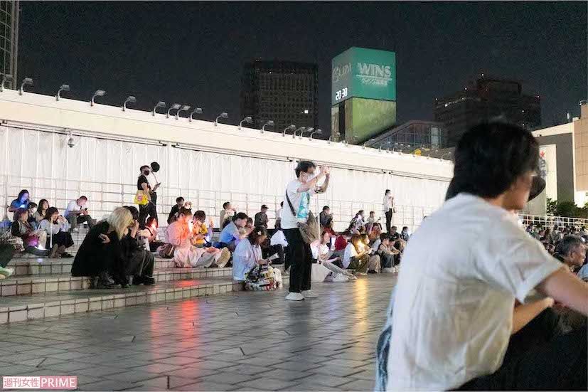 端に寄って、手元の媒体でライブを見届けるファンたち