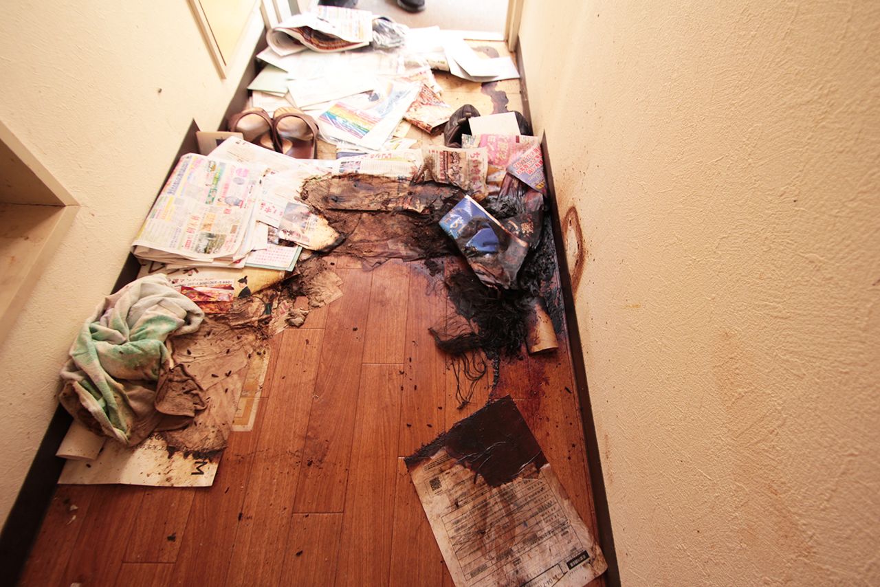 写真右側の黒い部分が髪の毛や血の塊。ここに男性の頭があった。吐血したと思われる血は玄関口（上のほう）に向かい流れていた。風呂場にも吐血した痕が