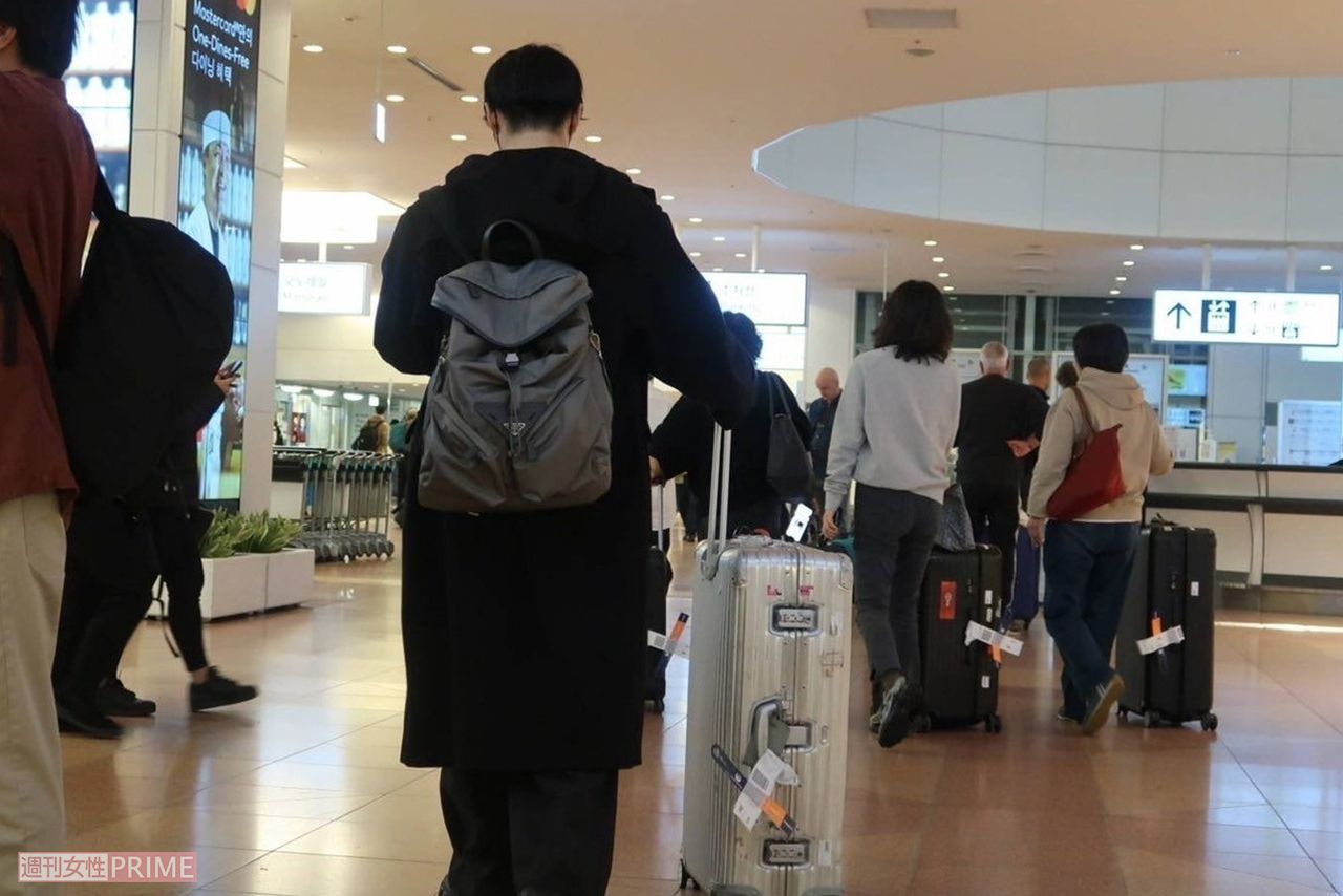 黄皓がシルバーのスーツケースを運ぶ後ろ姿