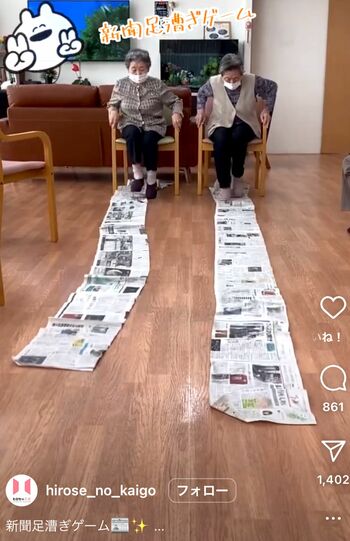 2人で競い合う「新聞足こぎゲーム」。座ったまま楽しめるため、保育園などからも取り入れたいとの声が（スマイルホーム豊栄インスタグラムより）